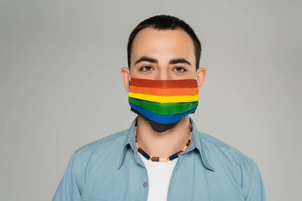 Portrait of brunette homosexual man in medical mask with lgbt flag isolated on grey — Stock Photo