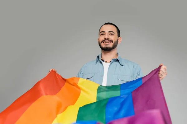 Alegre joven gay sosteniendo bandera lgbt aislado en gris, Día Internacional contra la Homofobia - foto de stock