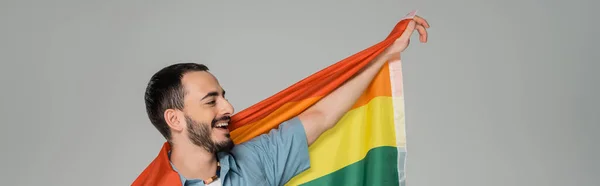 Щасливий гей-чоловік тримає прапор lgbt і дивиться ізольовано на сірому, банер — стокове фото