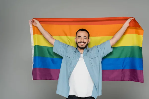 Giovane uomo omosessuale con bandiera lgbt e guardando la telecamera isolata sul grigio, Giornata internazionale contro l'omofobia — Foto stock