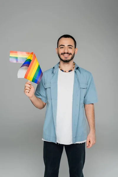 Smiling homosexual man holding lgbt flags and looking at camera isolated on grey — Stock Photo