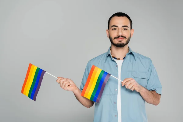 Retrato de un hombre gay barbudo sosteniendo banderas lgbt aisladas en gris, Día Internacional contra la Homofobia - foto de stock