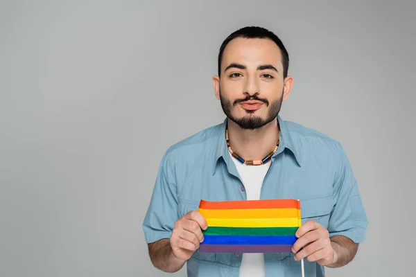 Morena gay hombre puchando labios y sosteniendo lgbt bandera aislado en gris, Día Internacional contra la Homofobia - foto de stock