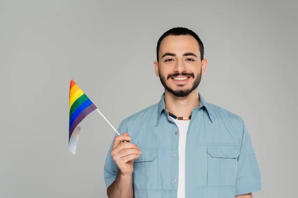 Portrait of smiling and bearded gay man in shirt holding lgbt flag isolated on grey, International Day Against Homophobia — Stock Photo