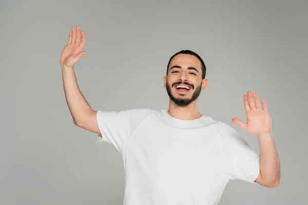 Cheerful gay man in white t-shirt waving hands at camera isolated on grey — Stock Photo