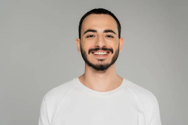 Porträt eines lächelnden schwulen Mannes im weißen T-Shirt, der isoliert auf grau in die Kamera blickt — Stockfoto