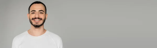 Giovane barbuto gay uomo in bianco t-shirt guardando fotocamera isolato su grigio, banner — Foto stock