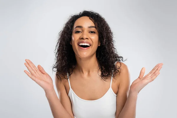 Impressed african american woman with wavy brunette hair showing wow gesture and looking at camera isolated on grey — Stock Photo