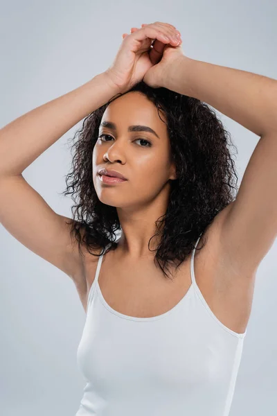 Портрет молодої афроамериканки з кучерявим брюнеткою волоссям позує руками над головою ізольовано на сірому — стокове фото