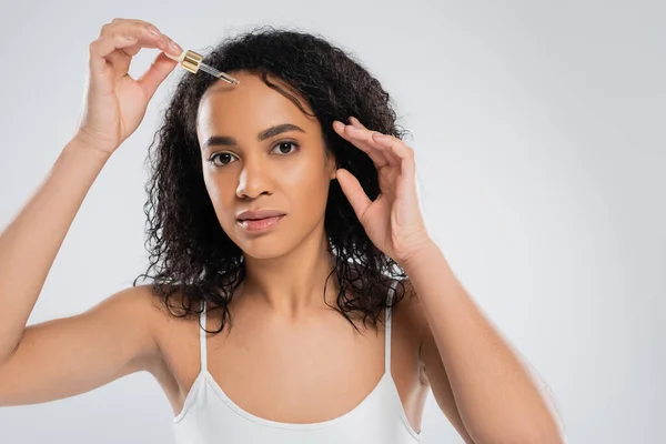 Bella donna afroamericana con pelle perfetta applicando siero cosmetico isolato su grigio — Foto stock