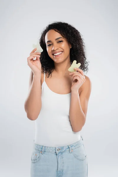 Брюнетка африканская американка держит каменные скребки и улыбается в камеру, изолированную на сером — стоковое фото