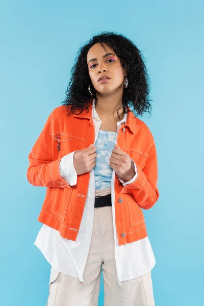Bella donna afro-americana in giacca arancione brillante guardando la fotocamera isolata sul blu — Foto stock