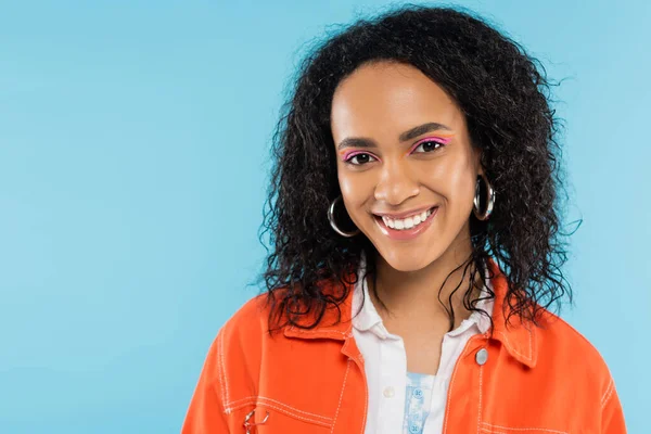 Porträt einer trendigen afrikanisch-amerikanischen Frau mit hellem Make-up, die isoliert auf blauem Grund in die Kamera lächelt — Stockfoto