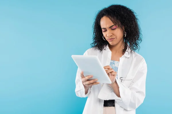 Displeased african american woman in white shirt using digital tablet isolated on blue — Stock Photo