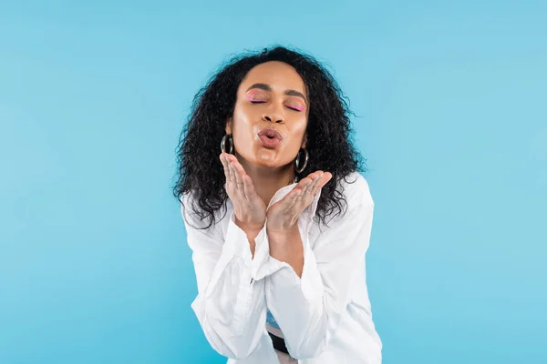Bella donna afroamericana con gli occhi chiusi soffiando aria bacio isolato su blu — Foto stock