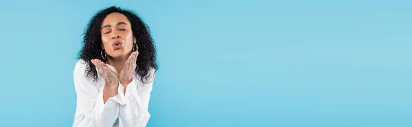 Brune afro-américaine avec les yeux fermés soufflant baiser d'air isolé sur bleu, bannière — Photo de stock