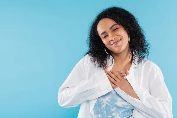 Pleased african american woman touching chest and smiling at camera isolated on blue — Stock Photo
