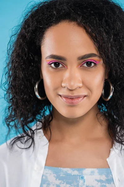 Retrato de mulher afro-americana positiva com cabelos encaracolados e brincos de argola isolados em azul — Fotografia de Stock