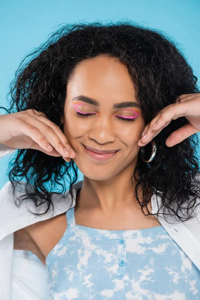 Porträt einer zufriedenen afrikanisch-amerikanischen Frau mit geschlossenen Augen, die ihr Gesicht isoliert auf blauem Grund berührt — Stockfoto