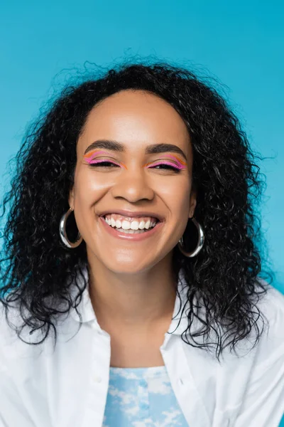 Porträt einer unbeschwerten Afroamerikanerin mit lockigem brünetten Haar, die isoliert auf blauem Grund in die Kamera lächelt — Stockfoto