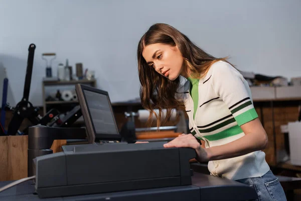 Pretty publishing worker looking at professional equipment in print center — Stock Photo