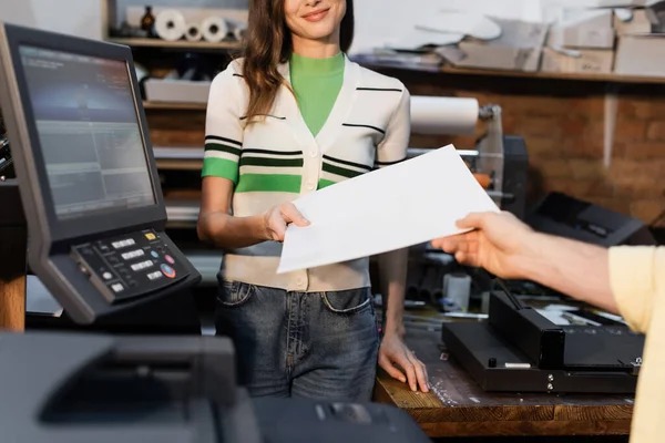 Cropped view of happy publisher giving blank paper to colleague in print center — Stock Photo