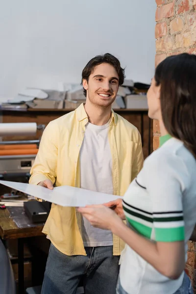 Homem alegre olhando para a mulher enquanto segurando papel em branco no centro de impressão — Fotografia de Stock
