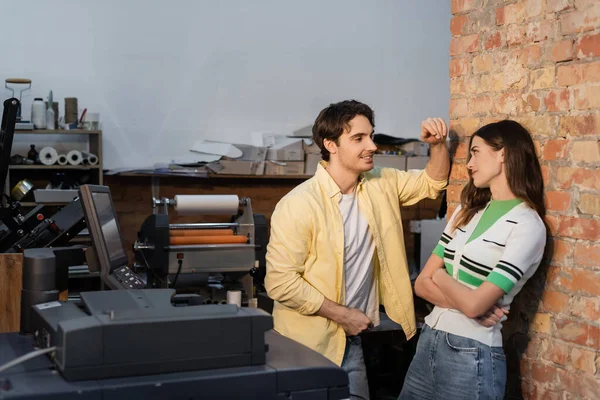 Fröhlicher Mann flirtet mit hübscher Kollegin, während er zusammen im Druckzentrum steht — Stockfoto