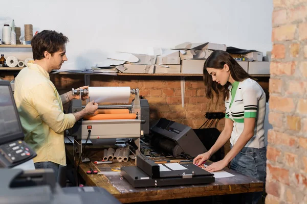 Mann steht neben Flexodruckmaschine und hübscher Kollegin im Druckzentrum — Stockfoto