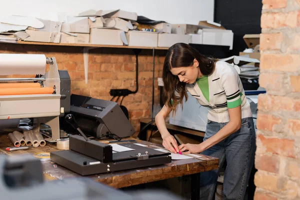 Busy typographer holding knife near paper while working in print center — Stock Photo