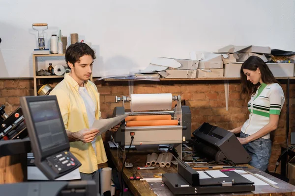 Good looking typographer looking at printed paper near pretty colleague — Stock Photo
