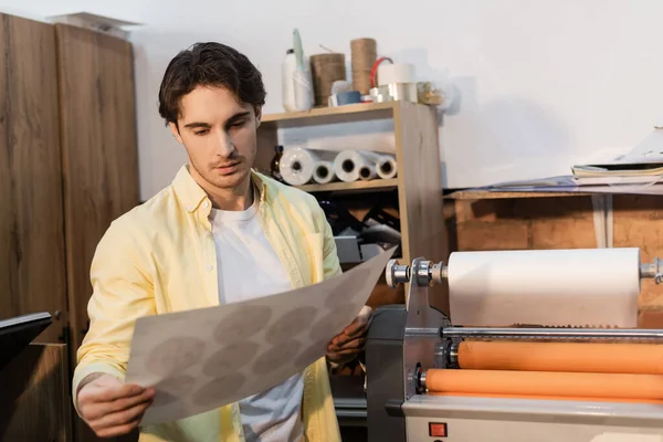 Tipógrafo mirando papel impreso cerca de plotter de impresión profesional - foto de stock