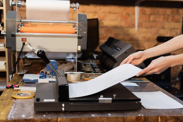 Обрезанный вид женщины, держащей бумагу возле триммера для бумаги в типографии — стоковое фото