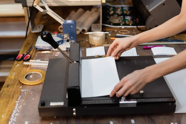 Vista cortada de mulher segurando papel ao lado de aparador no centro de impressão — Fotografia de Stock