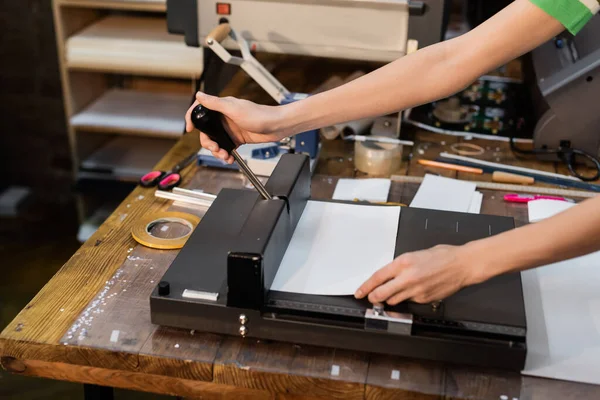 Zugeschnittene Ansicht einer Frau, die Papier schneidet, während sie Trimmer im Druckzentrum benutzt — Stockfoto