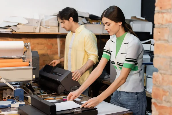 Pretty typographer using paper trimmer near colleague next to printer — Stock Photo