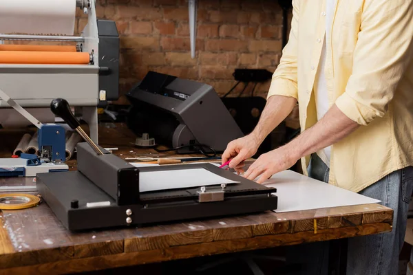 Ausgeschnittene Ansicht eines Typographen, der Papier mit Messer in der Nähe eines Papierschneiders im Druckzentrum schneidet — Stockfoto