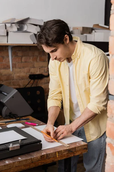 Gut aussehender Drucker mit Lineal und Bleistift in Papiernähe im modernen Druckzentrum — Stockfoto