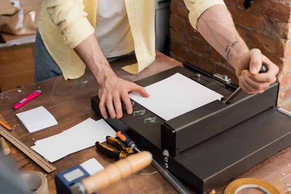 Vista ritagliata dell'uomo tatuato utilizzando la macchina per tagliare la carta nel moderno centro di stampa — Foto stock