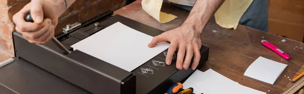 Vista recortada del hombre tatuado utilizando la máquina cortadora de papel en el centro de impresión moderno, pancarta - foto de stock