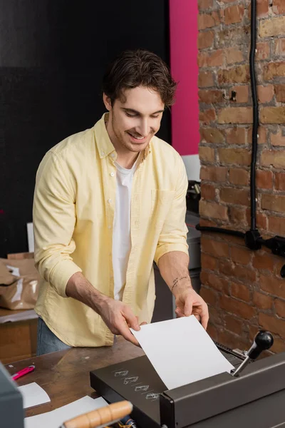 Homme tatoué heureux tenant du papier près de la tondeuse dans le centre d'impression moderne — Photo de stock
