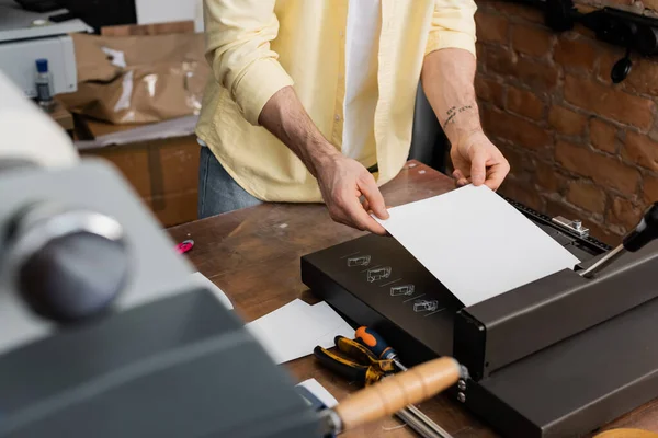 Vista cortada de homem tatuado segurando papel perto de máquina de aparador no centro de impressão moderna — Fotografia de Stock