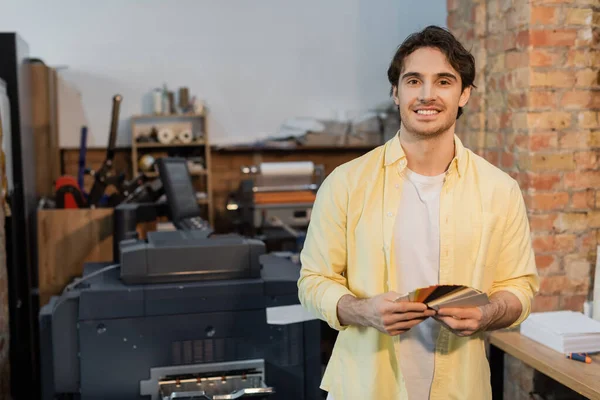 Homem feliz escolhendo a cor enquanto segurando amostras no centro de impressão moderno — Fotografia de Stock