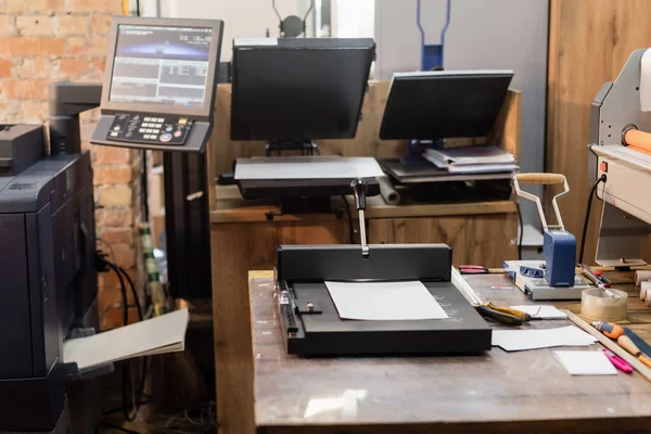 Centro di stampa con attrezzature moderne accanto al monitor e trimmer di carta — Foto stock