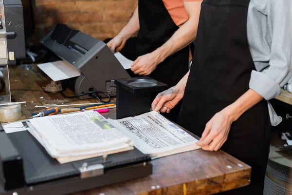 Vista cortada de jornais com notícias econômicas perto de homem e mulher que trabalham no centro de impressão — Fotografia de Stock