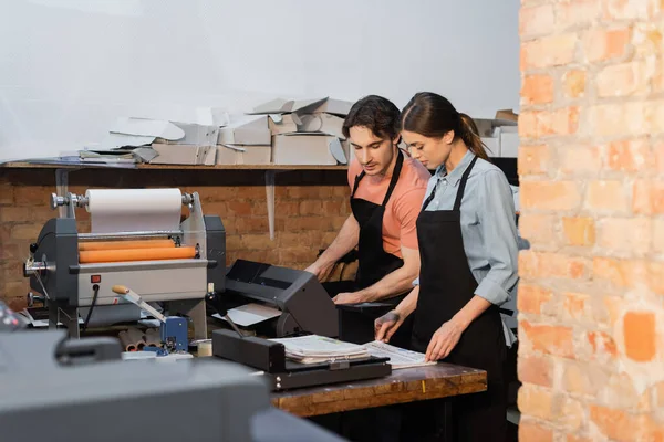 Typographers in aprons looking at newspapers while working in print center — Stock Photo