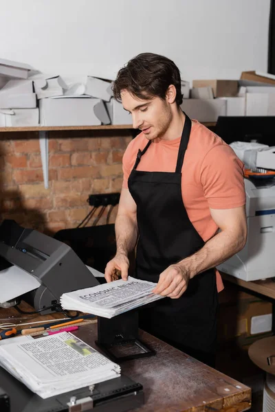 Good looking typographer looking at freshly printed newspapers with economic news — Stock Photo
