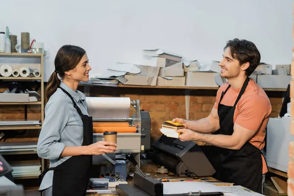 Cheerful man in apron showing color samples to pretty colleague in print center — Stock Photo