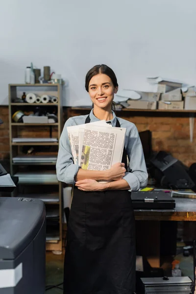 Восторженный типографша в фартуке держа свежие печатные газеты — стоковое фото