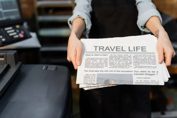 Partial view of typographer with tattoo on hand holding freshly printed newspapers — Stock Photo
